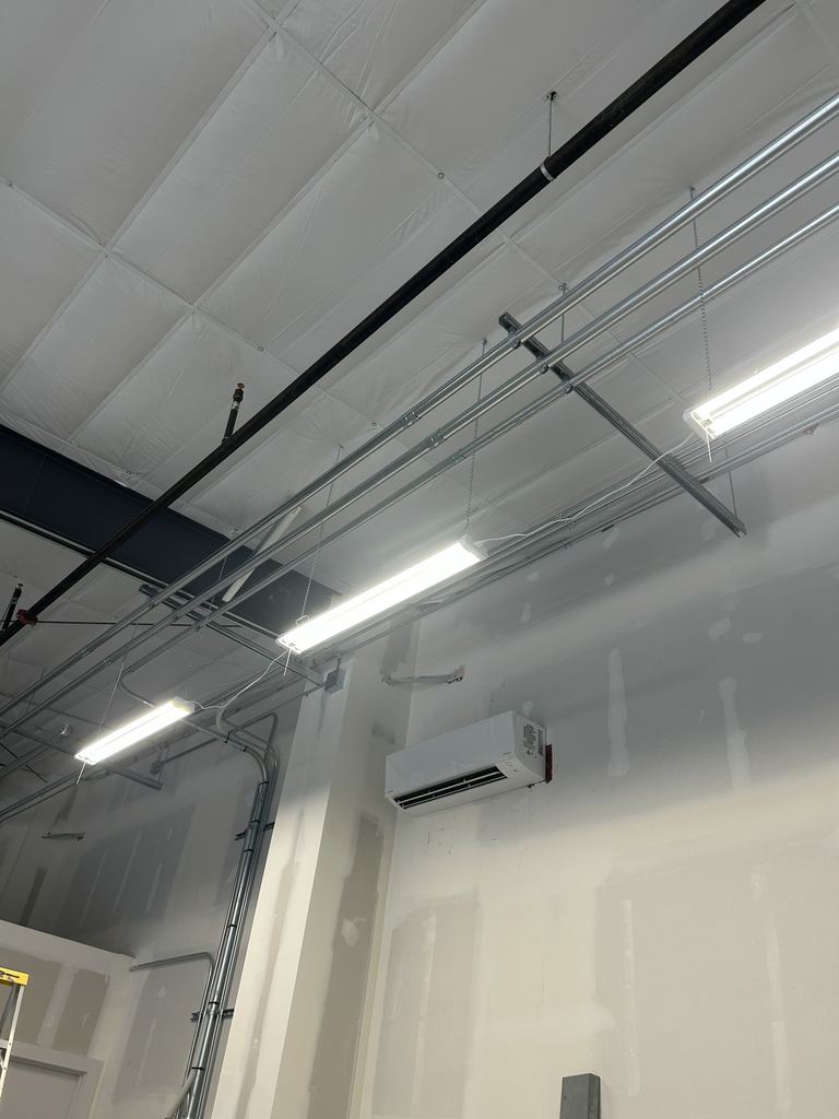 High commercial ceiling with parallel runs of metal conduit, LED strip light fixtures and a wall-mounted mini-split unit