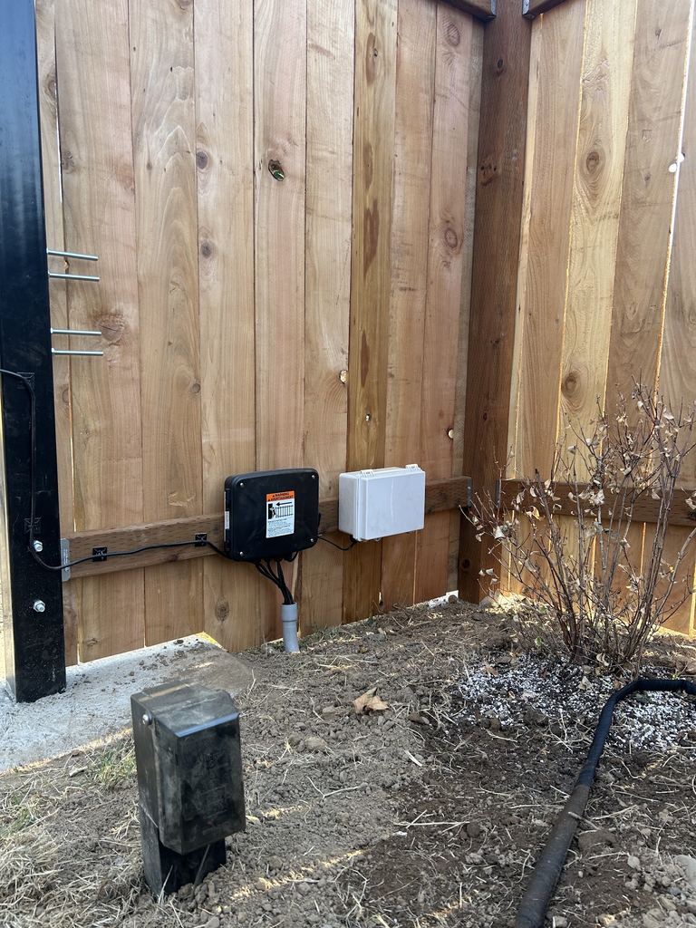 Gate operator control box and a weatherproof enclosure mounted on a cedar fence with conduit running to the ground