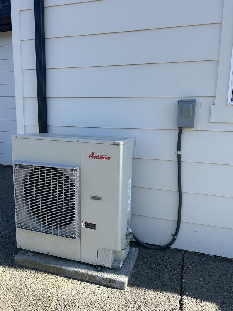 Outdoor heat pump unit beside a house with a disconnect box and flexible conduit on the wall