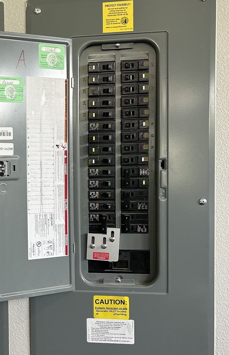 Open electrical panel with a generator interlock plate at the main breaker and a caution label noting a portable generator inlet