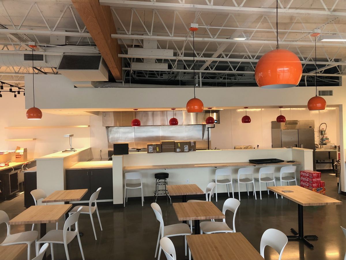 Restaurant interior with an open ceiling, orange pendant lights over the counter and track lighting