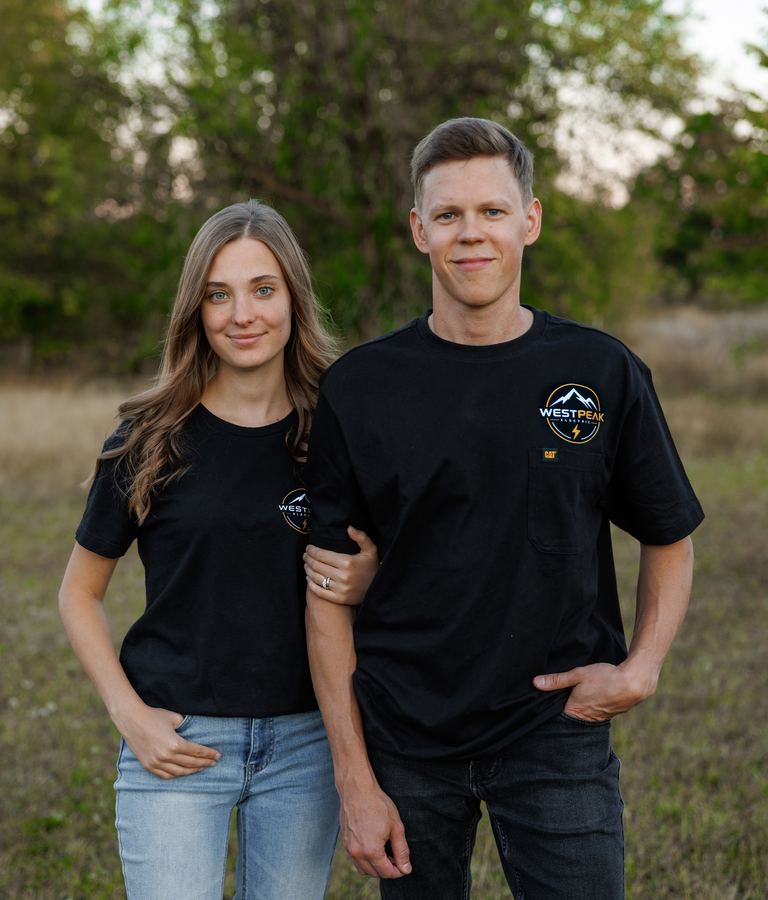 A man and a woman in black WestPeak Electric shirts standing outdoors